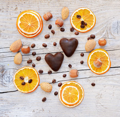two chocolate hearts, dried orange slices and nuts on wooden background