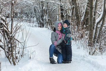 Fototapeta na wymiar Beautiful young mother walking with her son in the winter forest.