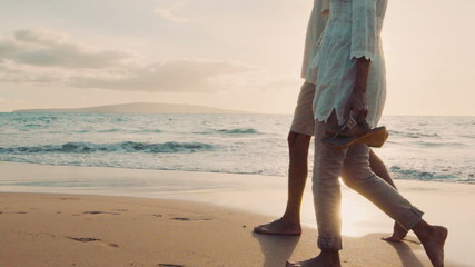 Sunset Walk on a Luxury Beach. Older Couple Holds Hands and Walks Down the Beach at Sunset Getting Their Feet Wet - Powered by Adobe