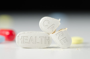 Stack of pills with HEALTH CARE stamped into them, the CARE pill is broken in half representing a broken Health Care system and bad medical care - obrazy, fototapety, plakaty