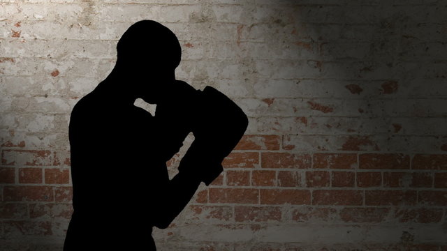 HD silhouette footage of a bald man wearing boxing gloves throwing various punches against a brick background