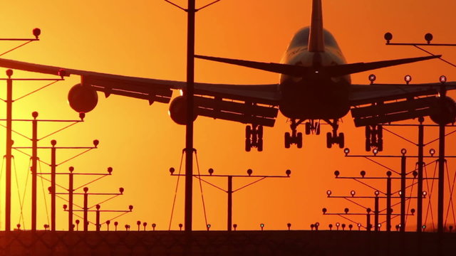 HD footage of a 4 engine jumbo jet plane landing in silhouette against an orange sunset sky, followed by a defocus / camera blur out.  Jet engine audio included.