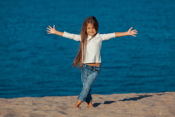 Fototapeta na wymiar Adorable happy smiling little girl on beach vacation. jeans.