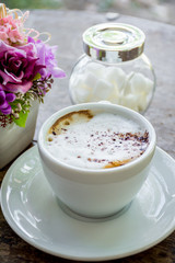 Hot cappuccino coffee with foam on top on wood table.