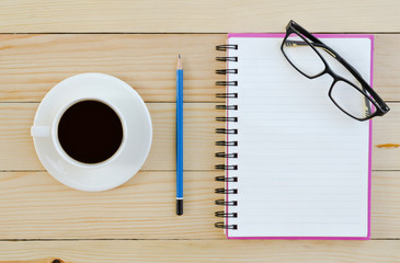 Blank white notebook with cup of coffee and pencil and glasses on the wooden table