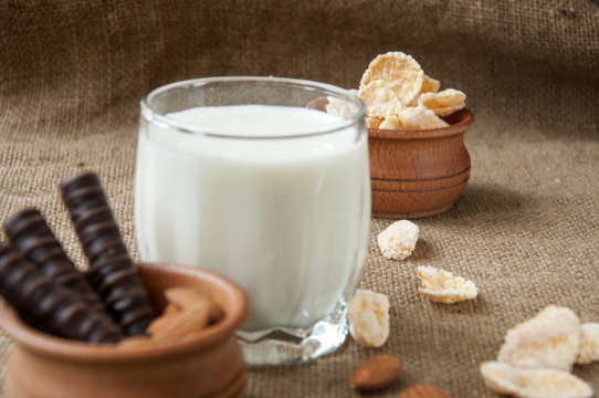 A glass of milk with almond nuts, corn flakes, chocolates,  on sacking, burlap background