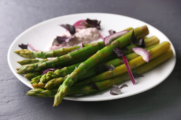 Fresh asparagus dish with red chopped onion on white plate against grey wooden background, close up