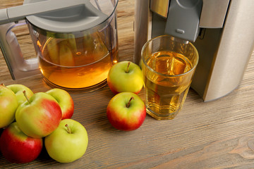 Stainless juice extractor with apples and glass of juice on wooden background, close up