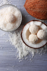 Candies in coconut flakes and fresh coconut on color wooden background