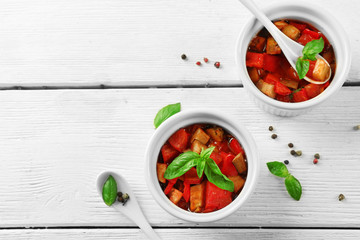 Tasty vegetarian ratatouille made of eggplants, squash, tomatoes in bowls on wooden table background