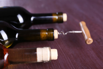 Three bottle wine and corkscrew on purple wooden background