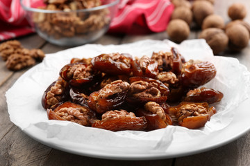 Walnut and date fruit in plate on wooden table, close-up