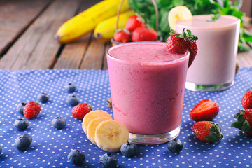 Glasses of fresh cold smoothie with fruit and berries, on blue tablecloth background