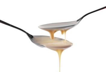 Condensed milk pouring from spoons, isolated on white