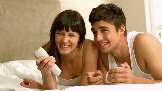 Happy young couple watching tv lying on bed