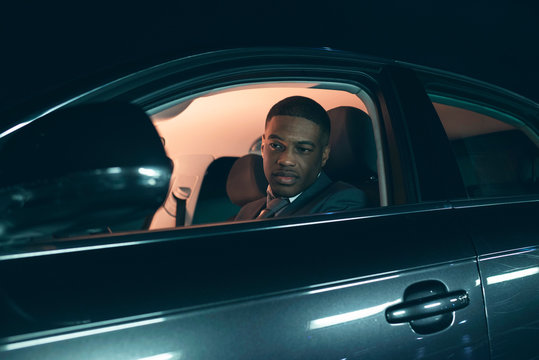 Young Hispanic Man Looking In Side Mirror Of Car At Night.