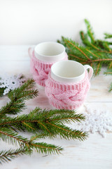 Obraz na płótnie Canvas Christmas tree and cup of hot tea in knitted cup holder on white wooden table