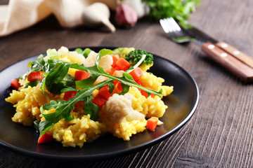 Black plate with vegetable risotto on served wooden table