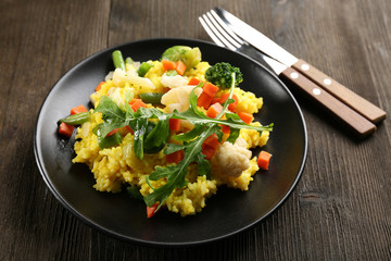 Black plate with vegetable risotto, fork and knife on wooden table