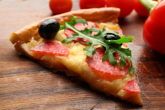 Delicious tasty piece of pizza with vegetables on wooden background, close up