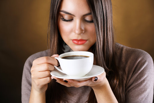 Woman holds cup of coffee and saucer in hands, close up