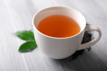 Ceramic cup of tea with scattered tea leaves around on light wooden background