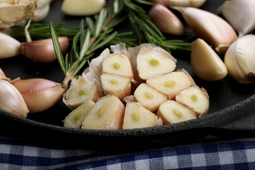 Fresh garlic with rosemary in black pan on blue checkered cotton napkin, close up