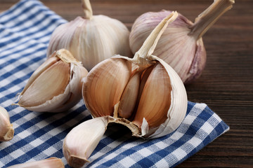 Fresh garlic on blue checkered cotton napkin on wooden background, close up