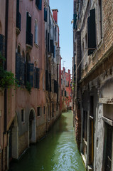 Fototapeta na wymiar Canal in Venice - old buildings, raw walls, closed shutters and doors near the water