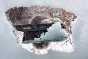 hand with brush cleaning window of car from the snow, closeup
