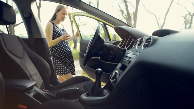 Pregnant woman sits in the car on the driver's seat and wear a safety belt