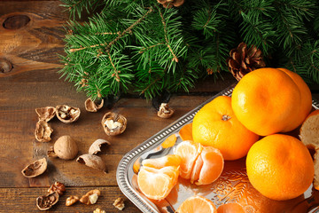 tangerines on an iron tray and a spruce branch with cone on wooden background