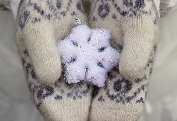 Female hands close up in knitted wore mittens holding white snowflake outdoors