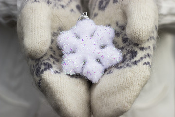 Fototapeta na wymiar Female hands close up in knitted wore mittens holding white snowflake outdoors