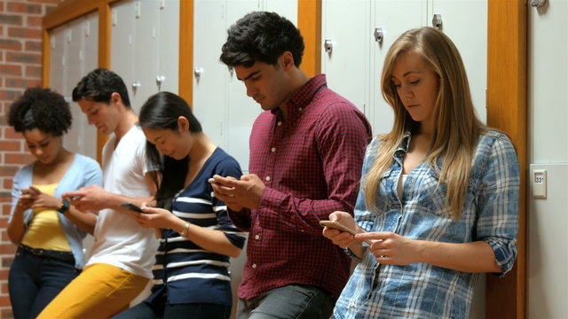 Students leaning against lockers using smartphones