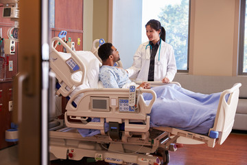 Female Doctor Talking To Male Patient In Hospital Bed