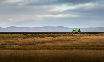 Lonely green roof cottage in yellow grass filed with mountain range background in Autumn season