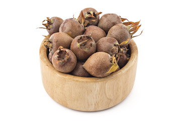 Wooden bowl filled with fresh organic medlars, isolated on white background