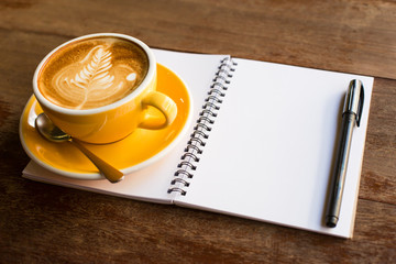 Hot latte art coffee cup on wooden table and note book.