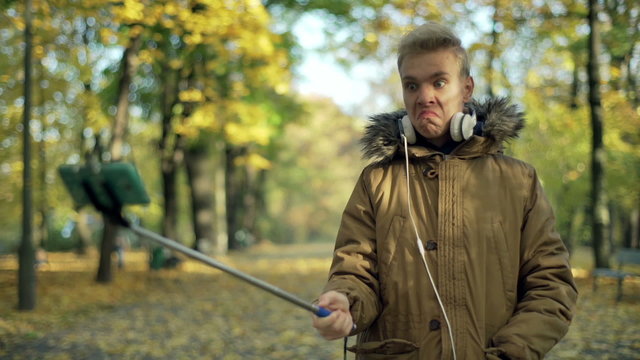 Man holding smartphone on selfie stick and doing funny photos in the park
