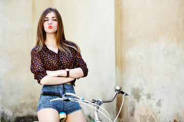 Charming girl woman with long hair is posing on the bicycle on the old wall background