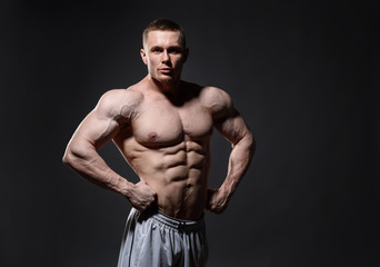 Fototapeta na wymiar Muscular man in studio over dark background shows his body 
