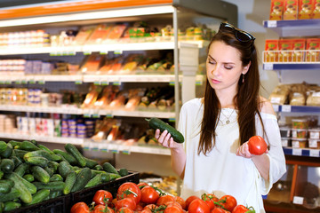 Young brunette girl is choosing cucumbers and tomatoes during shopping