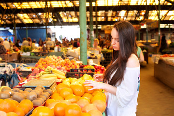 Young brunette woman is choosing oranges during shopping at fruit vegetable market