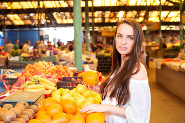 Brunette girl is holding oranges during shopping at fruit vegetable market