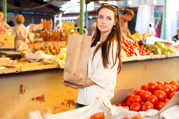 Pretty young woman with pack of products is standing near the counter with tomatoes