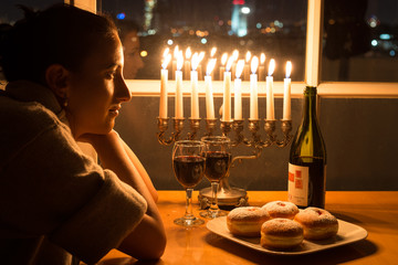 Girl sits by candles on Hanukkah holiday. Hanukkah celebration attributes. Judaic holiday of lights.