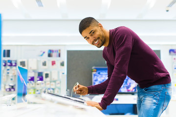 Handsome man looking for new tablet. He is using pencil for tablet computer. Tech shop.