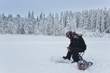 Fototapeta na wymiar Man is ice-fishing in Ruka in Lapland