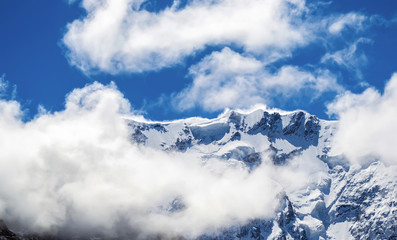 Fototapeta na wymiar Close view of snowy mountain ridge shrouded in clouds. Blue sky. Clear summit. North Caucasus.